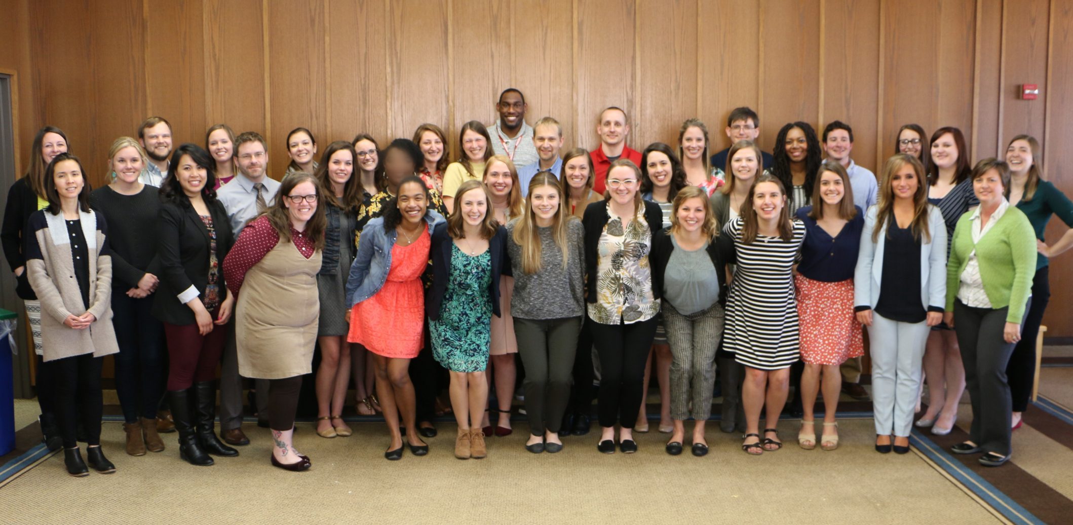 Cohort photo of 2016-2017 LEND trainees standing in a room with wooden boarded walls.